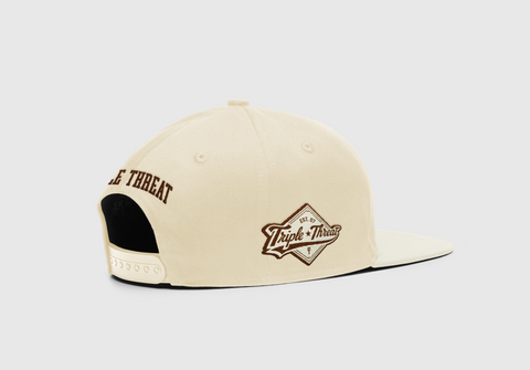 Side back view of Triple Threat cream snapback hat with "Triple Threat" in brown embroidered text at the back and the diamond Triple Threat logo on the right side of hat