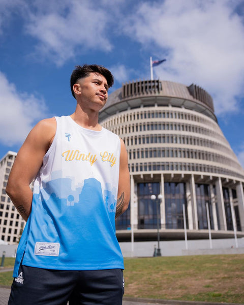 Model wearing Windy City singlet in white and blue, standing in front of the Beehive building in Wellington, New Zealand